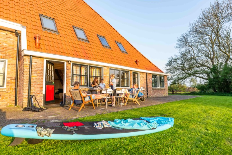 Mensen aan tafel op het terras bij De Koevoet, met een supboard op het gras